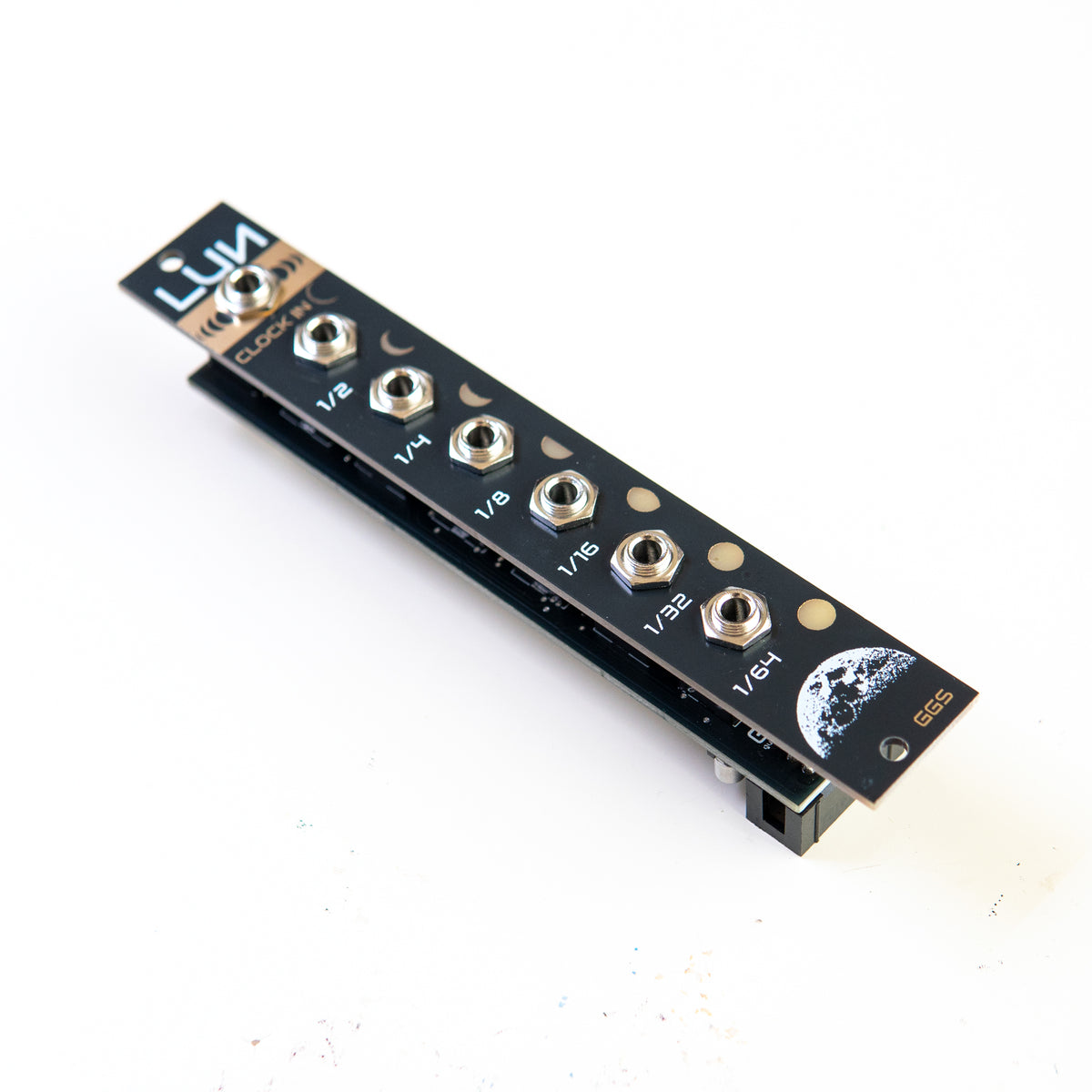 Eurorack clock divider module, LUN. angled photo with white background. black, white and gold (EING) PCB art fornt panel and jack sockets are visible. Moon theme in the design.