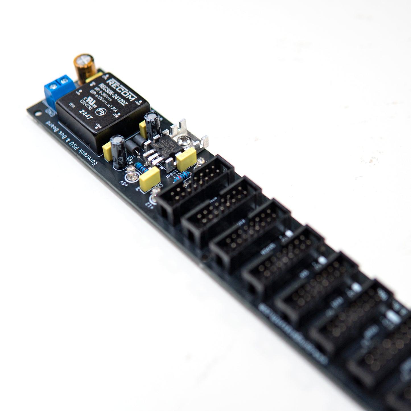 Eurorack power supply and bus board, power distribution. Synth PSU. +12V, -12V and +5V voltage regulator. Angled view. Electronic components visible.